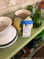 Close-up of ceramic pitchers and green glass bottles with lot label taped on pitcher