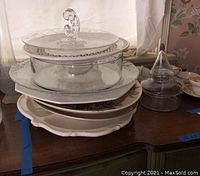 Stack of assorted ceramic platters with glass serving pieces on top