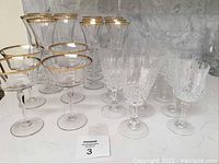 Full view of assorted Mikasa gold trimmed stemware plus crystal stemware glasses arranged on marble surface.