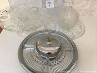 Glass and aluminum divided appetizer tray with domed lid and handle, set among multiple glass cake stands and candy dishes, all clear with starburst cut glass pattern.