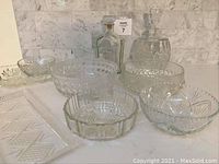 Front view of set showing two bottles, five bowls, and two platters with detailed patterned etching and cuts on clear glass/crystal pieces.