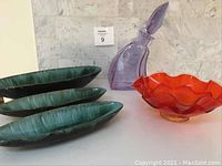 Three green pottery plates with a mottled glaze, shaped with organic leaf-like contours, alongside crystal decanter and orange bowl.