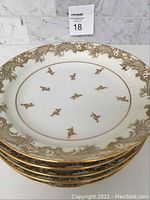 Stack of six white porcelain plates featuring gold Chambon pattern on rim