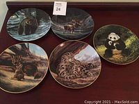 All five collector plates displayed on table showing wildlife scenes: grizzly bear, moose, red wolf, snow leopard and panda