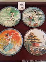 Four Bradford Exchange collector plates on a table: three with ladies in traditional attire, one with a temple.