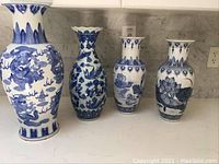 Front view of all four white ceramic vases with blue patterns, showing different shapes and designs including dragon and floral motifs.