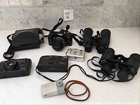 Overview of various vintage cameras and binoculars placed on a white surface showing condition and types included.