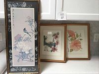 Four framed artworks arranged together on a counter, showing a traditional Asian style painting and two botanical prints.