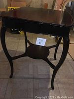 Full view of antique black table showing scalloped edges and curved legs.