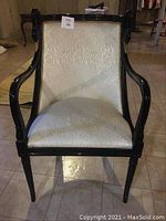 Front view of black lacquered wooden chair with ivory fabric upholstery and swan head designs on the armrests.