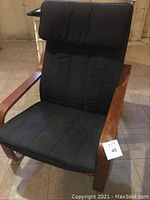 Front view of the chair showing dark black cushioned fabric with light wear, solid brown wooden arms and base.