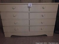 Front view of the chest showing 8 drawers and solid round handles, worn paint finish, and curved base detail