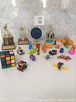 Full view of the lot showing hockey trophies, Rubik's cubes, and assorted toys arranged on a white surface against a tiled wall.