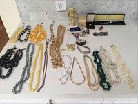 Table top display of assorted vintage costume jewelry including bead necklaces, chunky chain necklace, and several bracelets and pins.