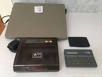 Franklin Computer Spelling Ace handheld device, Texas Instruments pocketbook, Melotone VHS tape rewinder, all electronics, with power cords and battery compartments visible