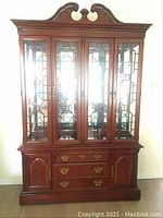 Front view of the mahogany china cabinet with carved top and glass paneled doors with decorative wooden mullions, showing internal shelves and lower drawers and doors.