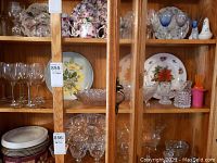 Full view of wooden cabinet shelf containing assorted glassware, crystal bowls, candleholders, and decorative plates on middle shelves.