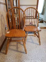 Front view of the two solid oak wooden dining chairs side by side showing curved slatted backrests, contoured seats and turned legs.