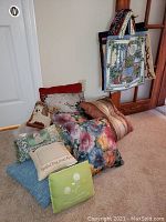 Various decorative cushions stacked and displayed with patterned quilted tote bags hanging behind them