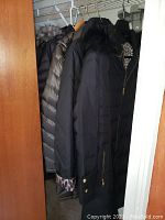 Photo showing multiple ladies coats hanging in a closet, showing fur trim and padded designs.
