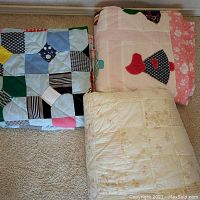 Three folded twin quilts showing different patterns: Dutch girl applique, colorful patchwork, and pink plaid.