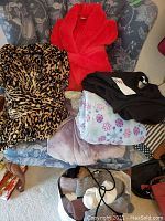 Full view of four robes and sleepwear folded on chair with bag of socks, showing leopard print, red, purple robes and floral fabric.