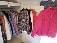 Wide view of multiple ladies jackets on hangers in various colors and styles including puffer, fleece, rain gear, and leopard print jacket.