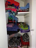 Multiple shelves filled with folded ladies scarves and pashminas in varying colors and materials, including reds, blues, purples, and animal prints, showing bulk of winter and seasonal scarves.