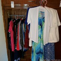 Wide view of summer weight ladies apparel on hangers showing dresses, cardigans, and pullovers in various colors including a white short sleeve cardigan and patterned dresses