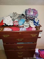 Full view of all loungewear items on top of and inside dresser including folded tops, slippers, socks, and dickies.