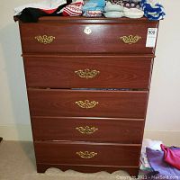 Front view of the five drawer dresser showing wood finish and brass handles, with some clothes on top.