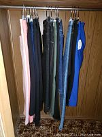 Photo showing multiple pairs of ladies pants hanging next to each other in various colors including pink, black, blue, olive, denim, bright blue.