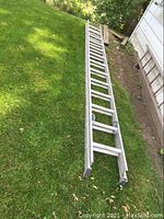Full length view of aluminum extension ladder laid on grass.