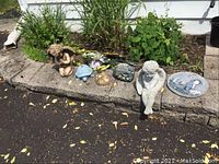 Wide shot of garden border with multiple concrete/resin small figurines and plaques arranged on stone ledge and soil