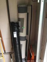 Rolled indoor/outdoor mat and Berber style carpet remnant standing upright.