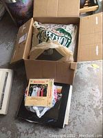 Open cardboard box showing assorted vinyl records, some with sleeves, others without. Boxes have thematic covers including a holiday-themed cover visible.