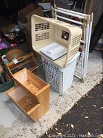 Lot of household organization and laundry items including a beige 60L plastic laundry hamper, white scale inside the hamper, white folding metal drying rack in background, and two wooden storage bins with two levels each one rectangular and one trapezoidal shape shows wear.