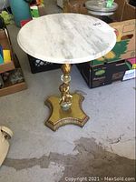 Full view of the round marble top table showing the white marble surface and the gold ornate pedestal base with decorative cherub figure and aged wear.