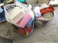 Two large plastic bags filled with assorted Tupperware and other storage containers in various colors including white, red, orange and clear. Bags show the containers packed densely.