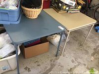 Two folding card tables side by side on concrete floor, blue and light beige tops visible