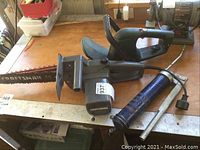 Craftsman electric chainsaw and grease tool on a wooden workbench, showing wear and brand names.