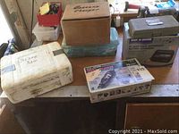 Overview of lot showing all items: Motomaster battery charger box, Ship N Shore battery charger metal case, white Sabre saw carrying case, Craftsman rotary tool kit box, plastic containers holding sockets and wrenches.