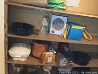 Shelf showing black speckled glass baking dishes, white Corning Ware casseroles, rustic slow cooker, electric heater, new oil lamp, and accessories.