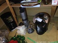 Keurig coffee maker with attached power cord, chrome pod holder, reusable and paper coffee filters placed nearby on a wooden floor