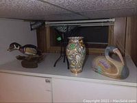 Wood duck, ceramic vase, and metal stand displayed on cabinet by a window