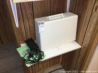 White hard plastic carrying case with handle, accompanied by foot pedal and user manual on a white surface against wood panel background.