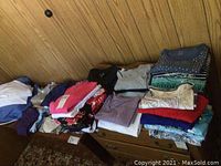Stacks of folded ladies shirts and sweaters in multiple colors and patterns on a dresser against a wood paneled wall.