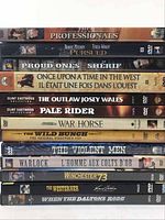 Stacked DVDs showing titles of Western movies including The Professionals, Pursued, The Proud Ones, The Sheriff, Once Upon a Time in the West, The Outlaw Josey Wales, Pale Rider, War Horse, The Wild Bunch, The Violent Men, Warlock, Winchester '73, The Westerner, When the Daltons Rode.