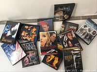 Photo of 13 DVD movie cases arranged in a pile, visible titles include The Good Thief, Infamous, Golden Door, Kiss Tomorrow Goodbye, White Dawn, Gran Torino, Out of Sight, Joe, Hanna, Pretty Poison, Tailor of Panama, Children of Men, and Monster Bob.