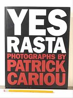 Front cover of 'Yes Rasta' photo book with bold white and red text on a black background: 'YES RASTA PHOTOGRAPHS BY PATRICK CARIOU'. Pencil shown for scale.